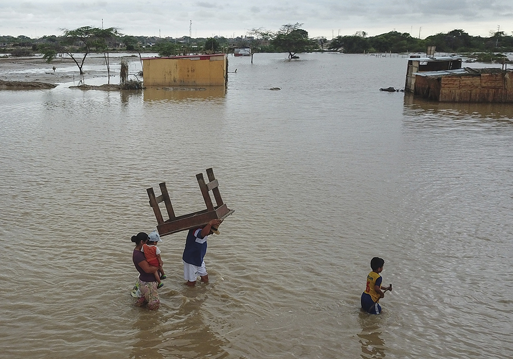A man carries a table through a street flooded by heavy rains of Cyclone Yaku, March 12, 2023, in Chiclayo, Peru. (AP photo/Aldair Mejia)