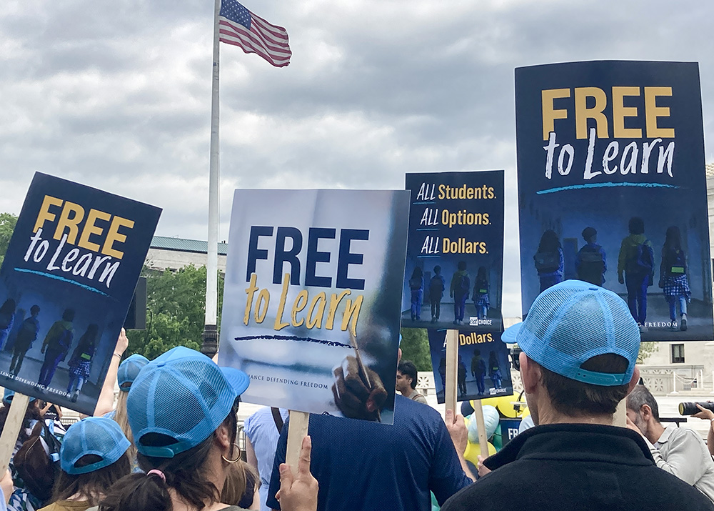 People gathered in front of the U.S. Supreme Court April 30 hold signs supporting that a Catholic charter school, St. Isidore of Seville Catholic Virtual School in Oklahoma, should get state taxpayer support. (NCR photo/Carol Zimmermann)