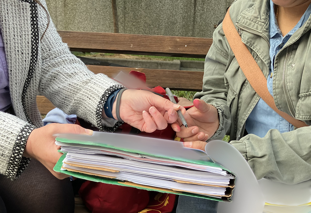 A woman and her attorney, at left, go over paperwork at the George H. Fallon Federal Building in Baltimore, a check-in field office for the U.S. Immigrations and Customs Enforcement. NCR accompanied the woman the day of her appointment. (Paperwork has been obscured digitally.) (NCR photo/Patricia Zapor)