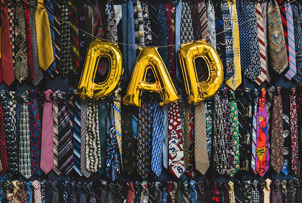 Gold balloon letters spell out "Dad" in front of a wall of ties (Unsplash/Tim Mossholder)