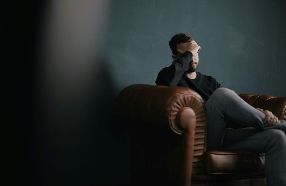 Person sits on couch, covering eyes.