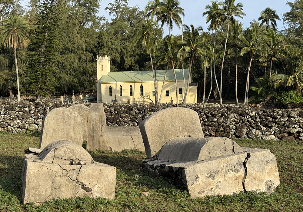 Graves are pictured at the Moku Puakala cemetery in Kalawao. In the background is the St. Philomena Catholic Church, St. Damien de Veuster’s main church which he helped to construct and expand, and the burial site of St. Damien. (National Park Service/Dewitt Jones) Graves are pictured at the Moku Puakala cemetery in Kalawao. In the background is the St. Philomena Catholic Church, St. Damien de Veuster’s main church which he helped to construct and expand, and the burial site of St. Damien. (National Park Service/Dewitt Jones)