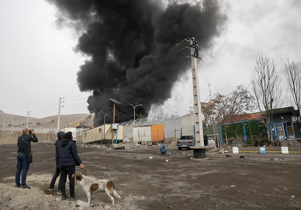 People look on and take photos as smoke rises after reported Israeli airstrikes on Shahran fuel tanks in Tehran, Iran, March 8, 2026, amid the U.S. and Israel-Iran war. (OSV News/WANA via Reuters/Majid Asgaripour)
