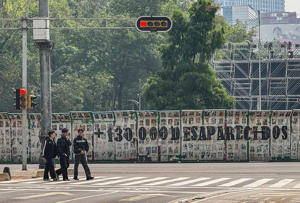 A group crosses Paseo de la Reforma in Mexico City July 6, 2026, near hundreds of photos of missing women, men and children, calling attention to the country's more than 130,000 disappeared. (GSR photo/Rhina Guidos)