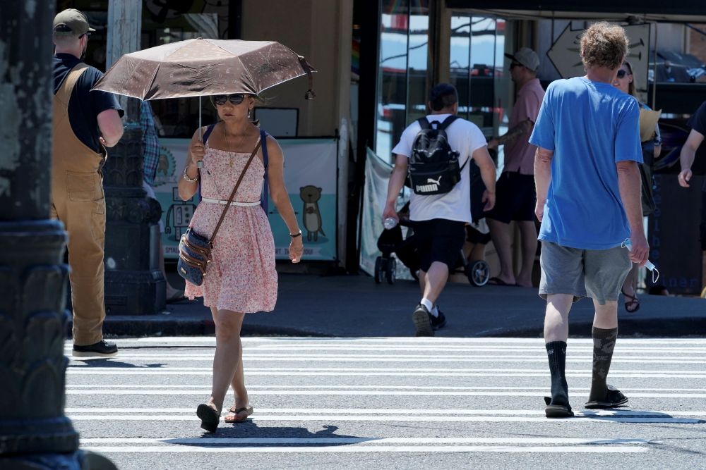 A person uses an umbrella for shade from the sun while walking near Pike Place Market June 29, 2021, in Seattle. The unprecedented heat dome that summer baked the Pacific Northwest for weeks in record-breaking extreme heat. More than 650 people died across the U.S. and Canada, including at least 19 in Spokane. (AP/Ted S. Warren)