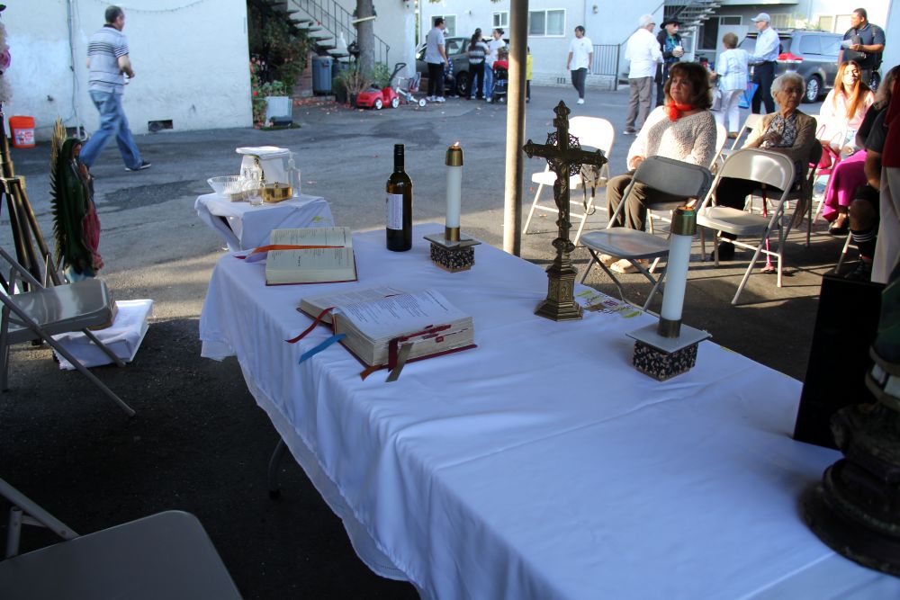 Neighborhood residents gather before an altar set up in a carport at a low-rise apartment complex for a "Misa Del Barrio," or "Neighborhood Mass," in Campbell, California, Aug. 21, 2026. A statue of Our Lady of Guadalupe stands behind the altar. (Marissa Nichols)