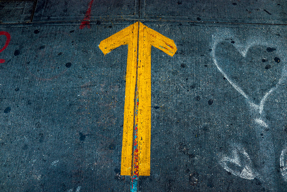 Yellow arrow and white spray-painted hearts on pavement (Unsplash/Jon Tyson)