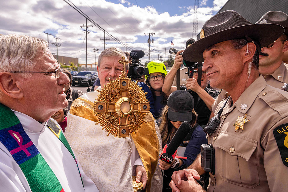 A member of the Illinois State Police, right, relays the message to clergy that U.S. Immigration and Customs Enforcement denied them access to detainees to provide Communion, outside an ICE facility in Broadview, Ill., Oct. 11, 2025. (AP/Adam Gray)