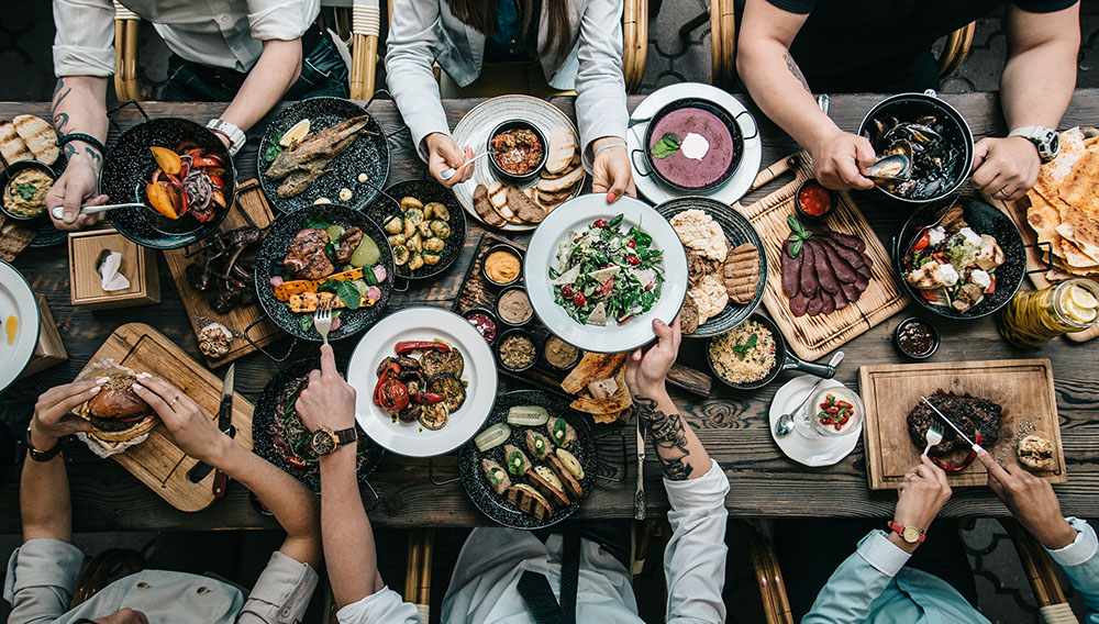 People eat and reach for food at a banquet table, viewed from above (Dreamstime/Olga Klochanko)