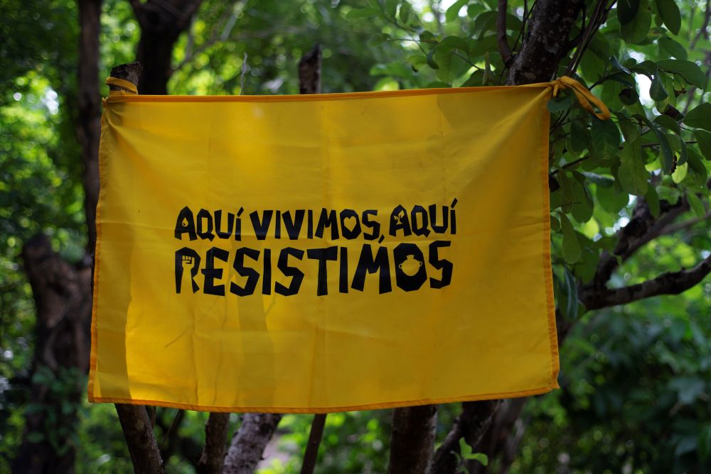 A banner with the message, "We live here, we resist here," was placed among the branches of a tree in the San Francisco Angulo community on Sept. 26. (Lissette Lemus) 
