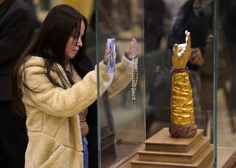 A woman prays in front of a glass-encased reliquary containing a bone from the arm of St. Jude the Apostle at St. Jude Church in Mastic Beach, N.Y., Nov. 27, 2023. (OSV News/Gregory A. Shemitz)