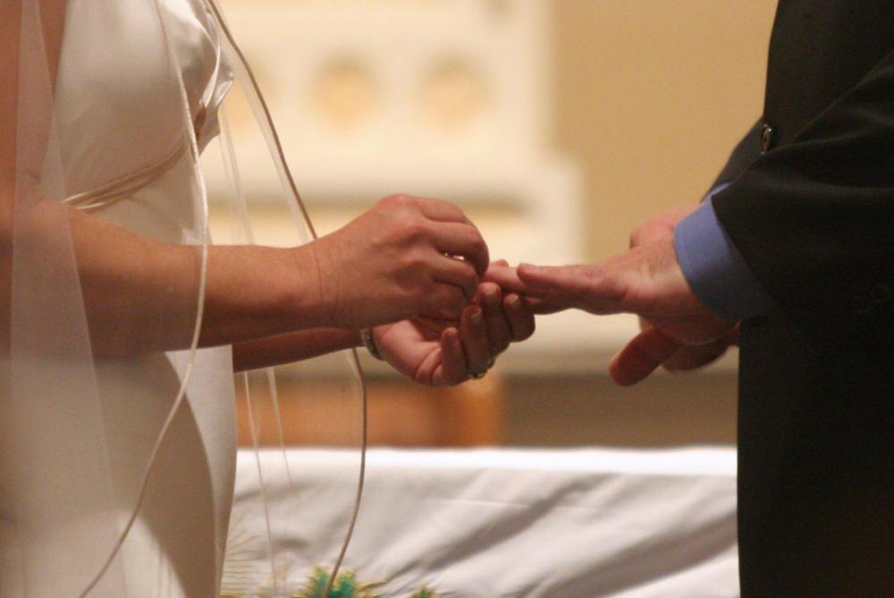 A bride places a ring on her groom's finger during their wedding