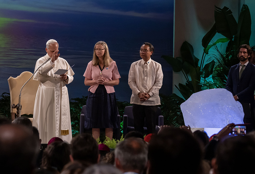 Pope Leo XIV offers a blessing at an international conference celebrating the 10th anniversary of Pope Francis' encyclical "Laudato Si', on Care for Our Common Home," at the Mariapolis Center in Castel Gandolfo, Italy, Oct. 1, 2025. To the right of Leo are Lorna Gold, Laudato Si' Movement executive director, and Yeb Saño, board chair of the movement, which organized the conference. In front of them is a chunk of ice from a glacier in Greenland. (CNS/Pablo Esparza)