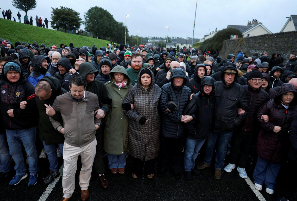 A large crowd of people standing shoulder to shoulder in cold, wet weather to block the road