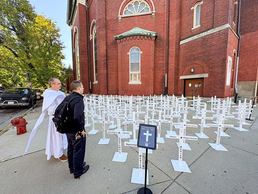 Dominican Fr. Brendan Curran, of Priests for Justice for Immigrants, and Fr. Thomas Boharic, pastor of Mother of the Americas Parish, stand by the traveling installation of immigrant crosses outside the church in Chicago's Little Village neighborhood, Oct. 3, 2026. (NCR photo/Camillo Barone)