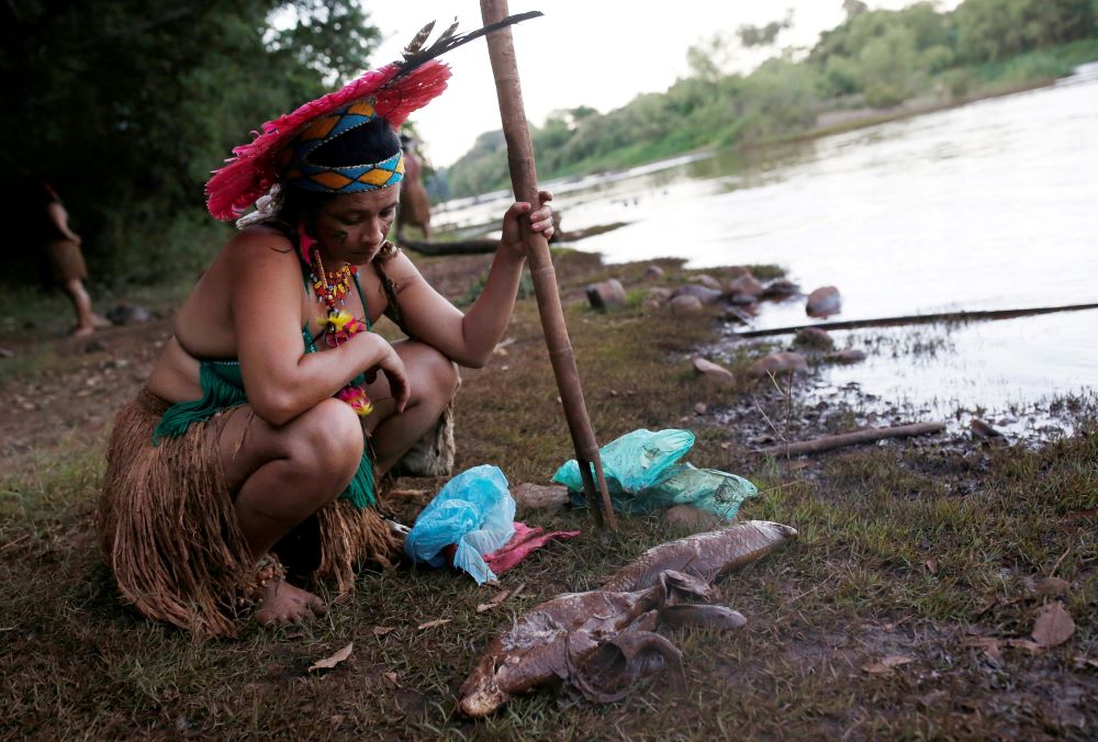 A woman from the Pataxo Ha-ha-hae tribe looks at dead fish near the Paraopeba River after a tailings dam owned by Brazilian mining company Vale SA collapsed near São Joaquim de Bicas, Brazil, in this Jan. 28, 2019 photo. (CNS/Reuters/Adriano Machado)
