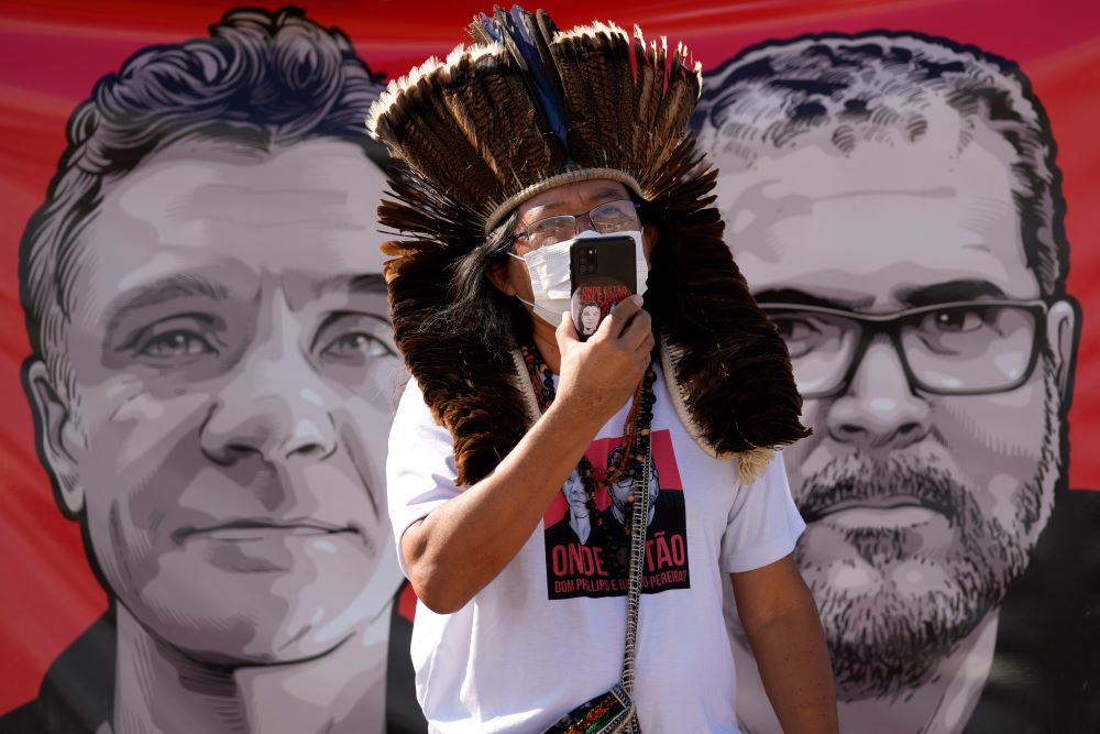 Indigenous leader Kamuu Wapichana stands in front of a banner that show images of missing freelance British journalist Dom Phillips, left, and Indigenous expert Bruno Pereira, during a protest.