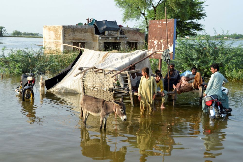 People wade in floodwaters outside their home, following heavy rains during the monsoon season in Sohbatpur district of Pakistan, Aug. 28. Experts say about one-third of the country is under water. (CNS/Reuters/Amer Hussain)