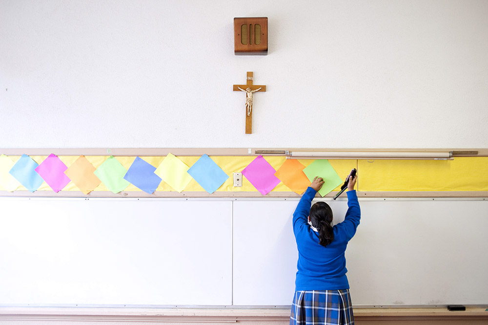This July 18, 2012, file photo shows a student stapling colored paper to the wall of a classroom after summer school at Our Lady of Lourdes in Los Angeles. (AP Photo/Grant Hindsley)