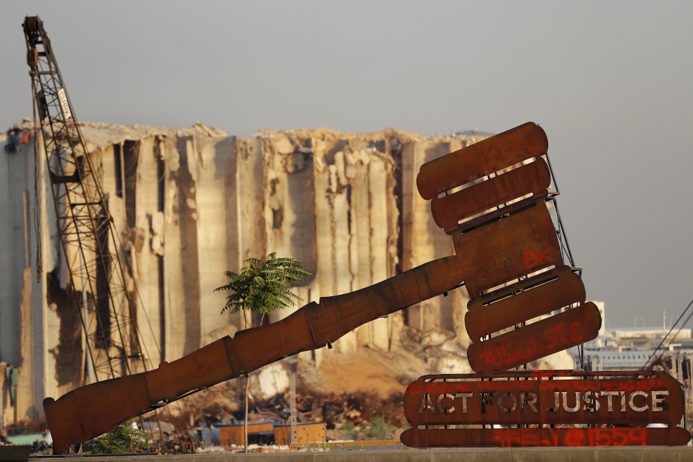 A justice symbol monument is seen Aug. 4 in front of towering grain silos that were gutted in the massive August 2020 explosion at the port that claimed the lives of more than 200 people, in Beirut, Lebanon. (AP/Hussein Malla)