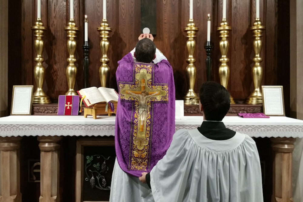 A priest elevates the Eucharist after consecrating it during a Latin Mass. (Creative Commons/Andrew Gardner)