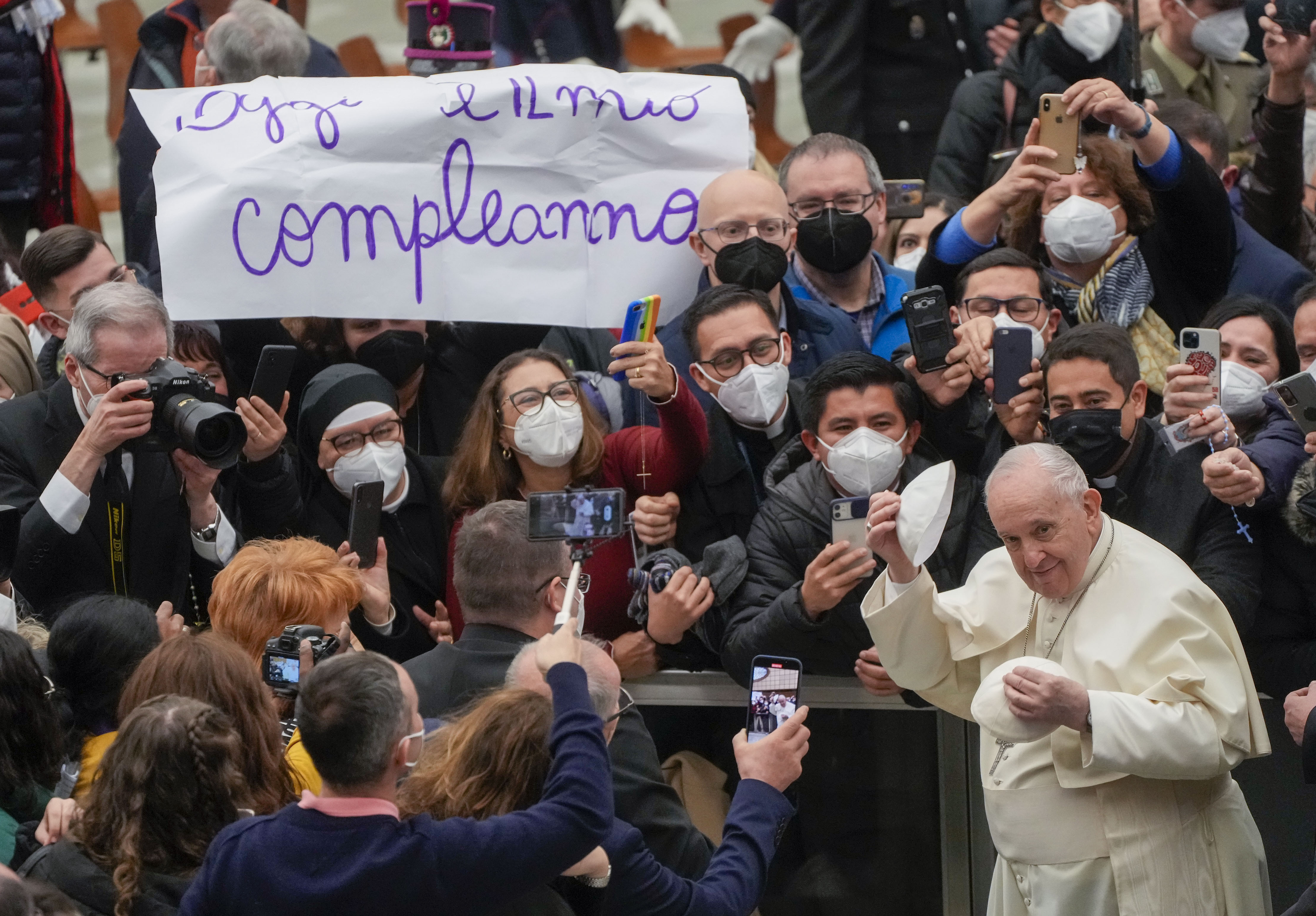 Pope Francis puts on a skull cap he was just presented with as he walks by a placard in Italian reading : "Today is my birthday", at the end of his weekly general audience in the Paul VI Hall at the Vatican, Wednesday, Feb. 02, 2022. (AP Photo/Gregorio Bo