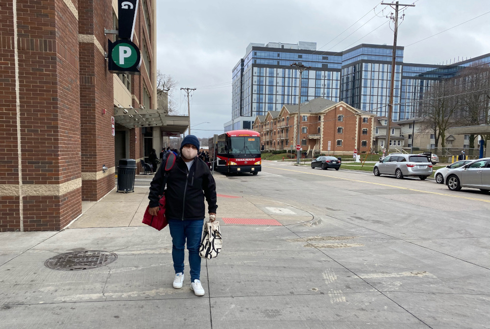 Man in a mask walking along a sidewalk toward camera