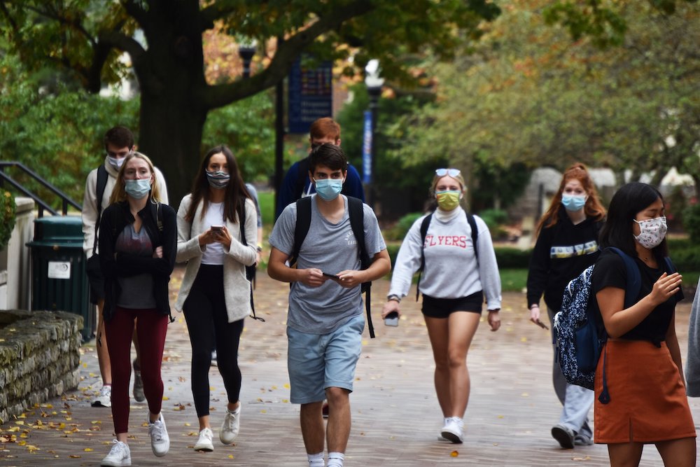 College students wearing masks walk side by side on a college campus