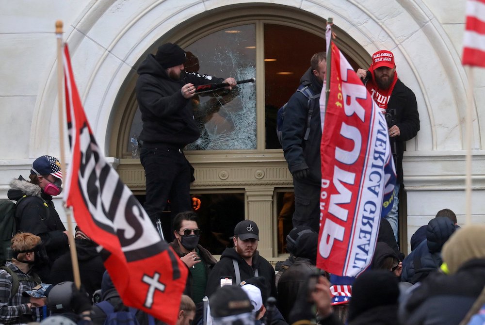 People carry flags with words "Jesus" and "Trump" on them as a President Donald Trump supporter breaks a window at the U.S. Capitol in Washington Jan. 6, 2021. (CNS photo/Leah Millis, Reuters)