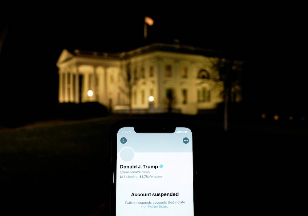 A smartphone showing the suspended Twitter account of President Donald Trump Jan. 8, 2021, is held up showing the White House in Washington in the background. (CNS/Reuters/Joshua Roberts)