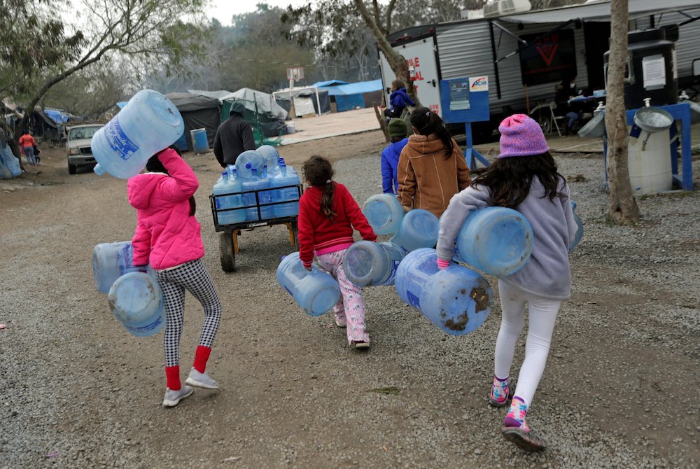 Children carry empty water containers inside a migrant encampment in Matamoros, Mexico, Feb. 18, 2021. (CNS/Reuters/Daniel Becerril)