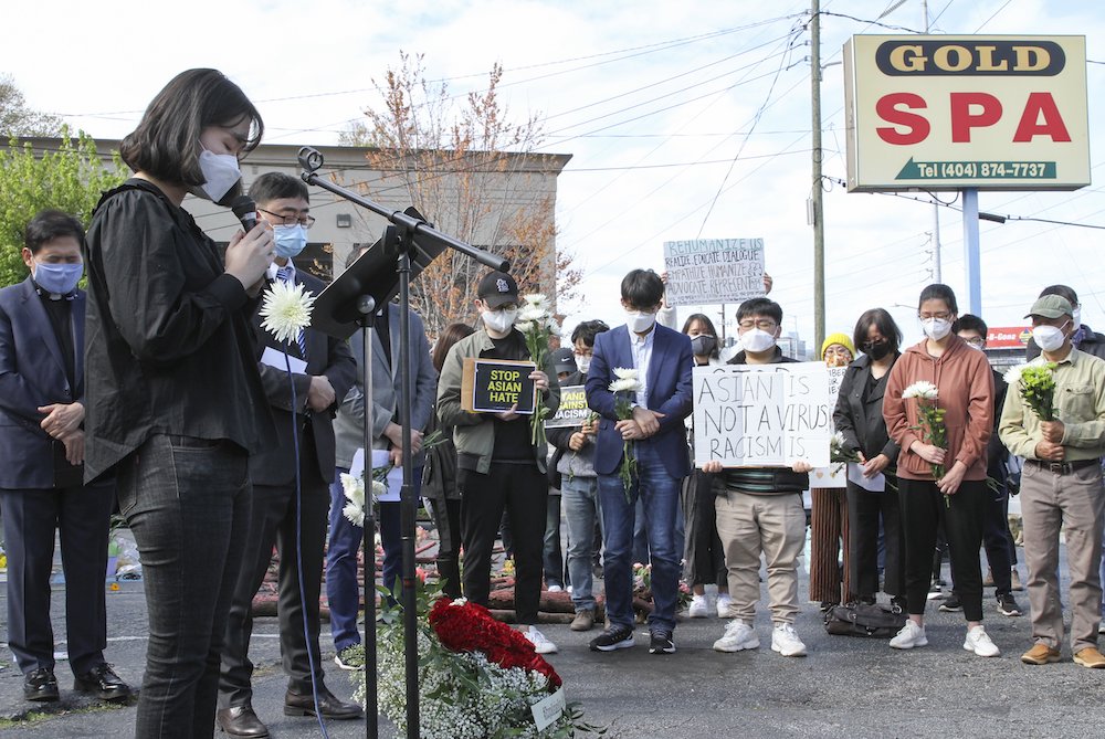 A group of mostly Asian and Pacific Islander people gather outside under a sign reading "Gold Spa" to pray