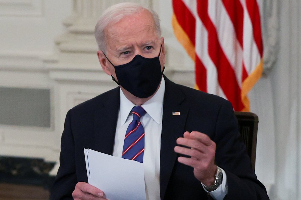Joe Biden seated in black mask holding papers