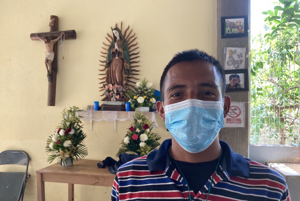 Young man in a mask posing inside with a crucifix and Virgin of Guadalupe in the background