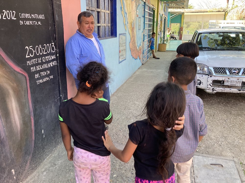 Children talking to a priest on a street by a colorfully painted wall