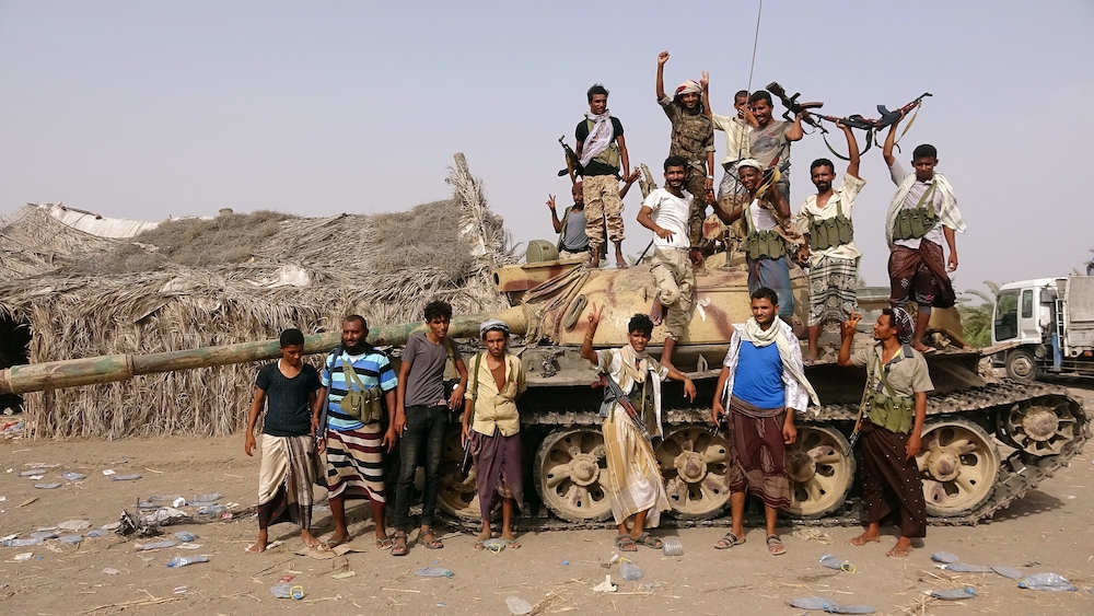 Tribal fighters loyal to the Yemeni government pose for a photo by a tank near Hodeida, Yemen, June 1, 2018. There are flattened plastic water containers strewing the ground. (CNS/Reuters/Stringer)