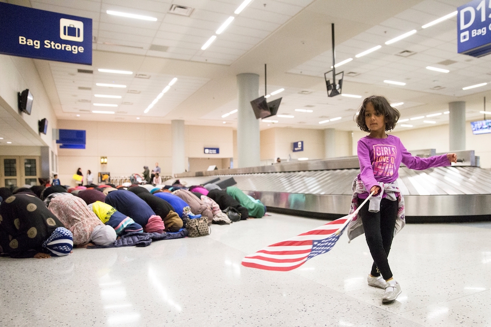 A young girl dances with an American flag at Dallas/Fort Worth International Airport in Dallas Jan. 29, 2017, as women pray during a protest against a travel ban imposed by U.S. President Donald Trump's executive action. (CNS/Reuters/Laura Beckman)