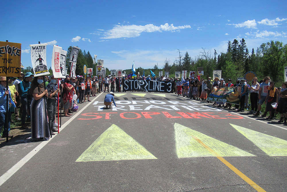 A man chalks an enormous message to President Joe Biden during a protest June 7 against the Enbridge Line 3 pipeline. (Claire Schaeffer-Duffy)