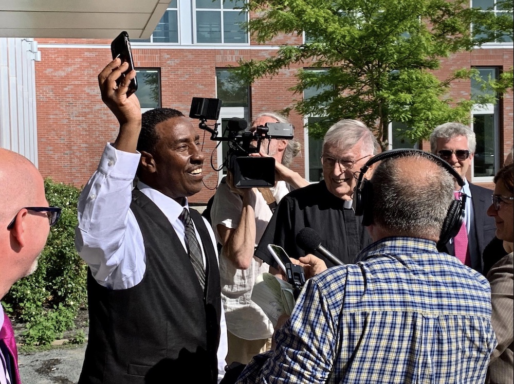 Jesuit Fr. Bill Barry, center, in clerical collar, joins Darrell Jones, left, holding up phone, in celebrations after Jones was found not guilty of murder on June 12, 2019, after being wrongfully kept behind bars for more than 30 years. (NCR photo/Bill Mi