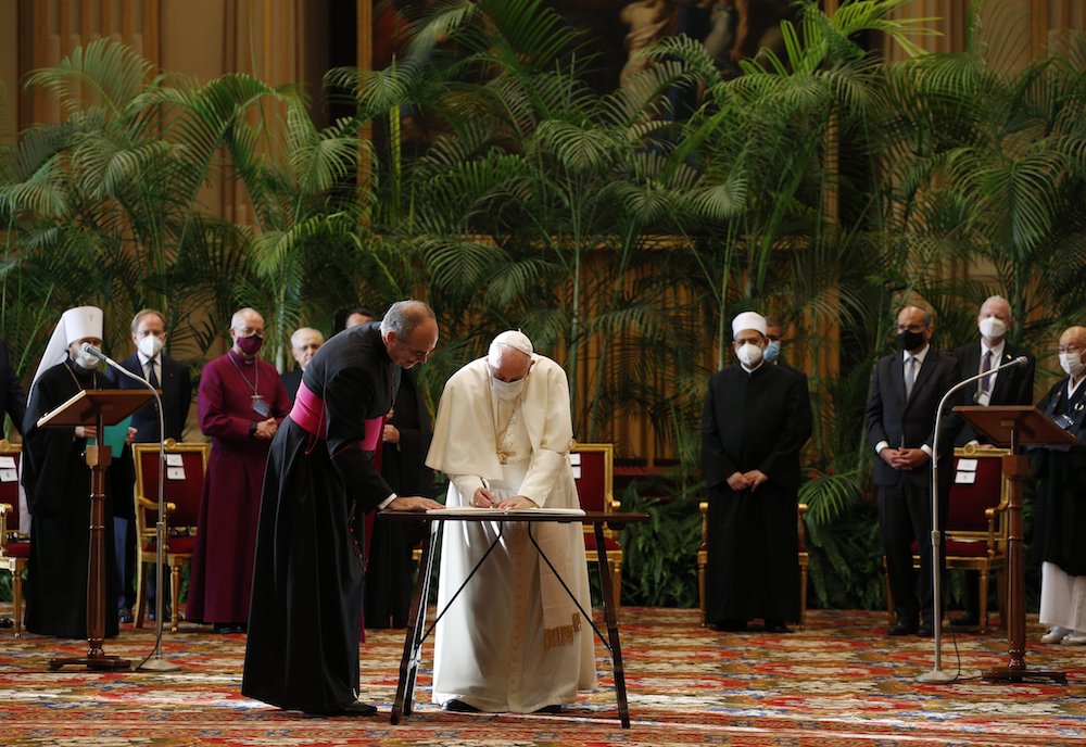 Flanked by leaders of major world religions Oct. 4 at the Vatican, Pope Francis signs a joint appeal to government leaders to curb global warming and heal the planet. (CNS/Paul Haring)