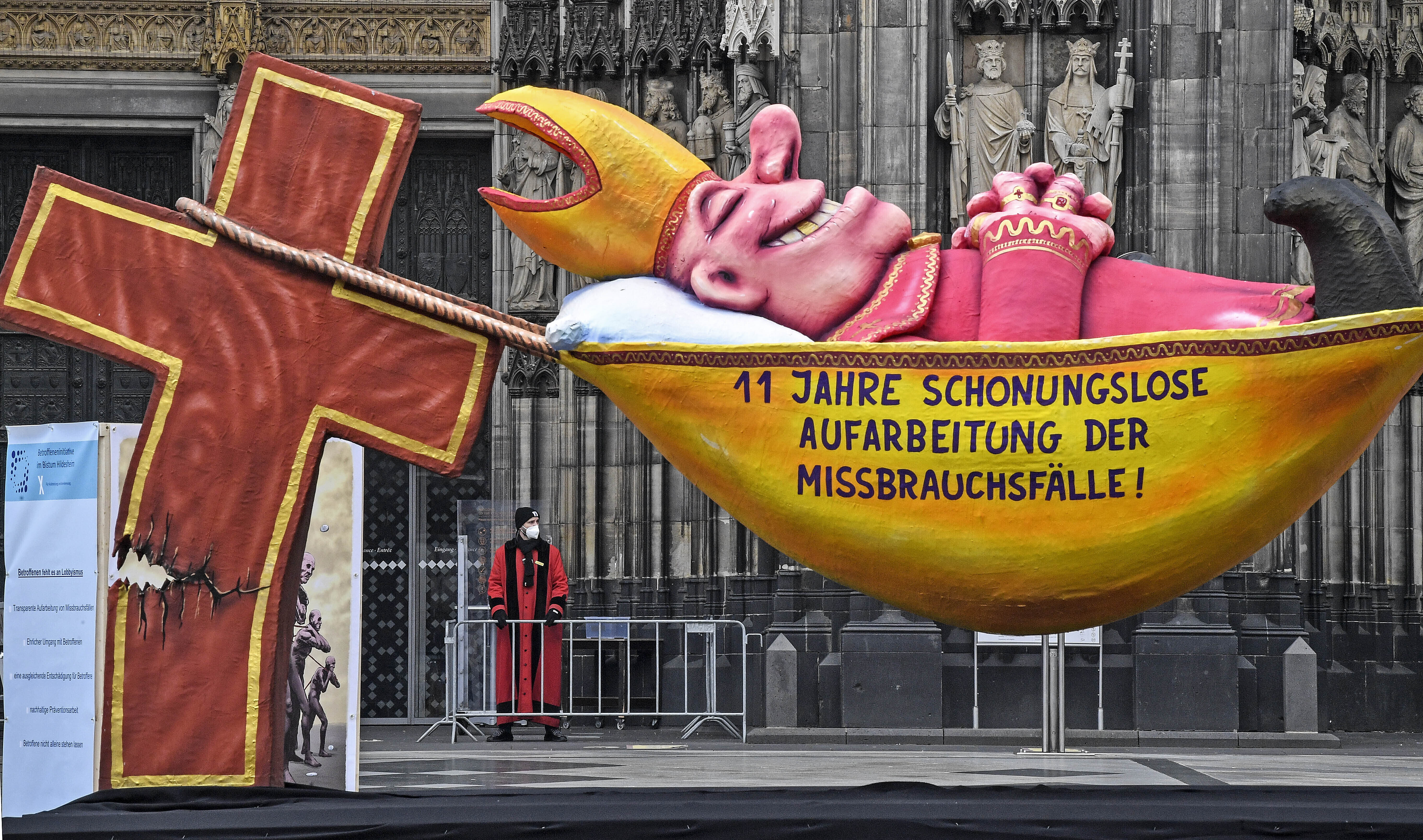 A carnival float depicting a sleeping Cardinal, reading '11 years of relentless processing of cases of abuse' is set in front of the Cologne Cathedral to protest against the Catholic Church in Cologne, Germany, Thursday, March 18, 2021. (AP Photo/Martin M