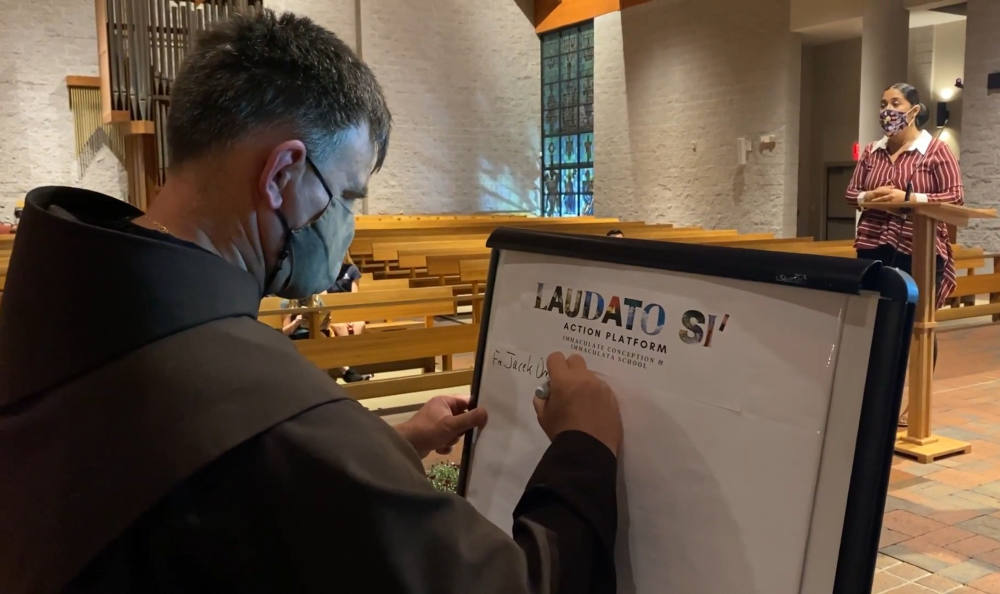 Franciscan Fr. Jacek Orzechowski, pastor of Immaculate Conception Catholic Church, in Durham, North Carolina, signs onto a pledge for the parish to join the Vatican's Laudato Si' Action Platform during an event in December. (NCR screenshot)