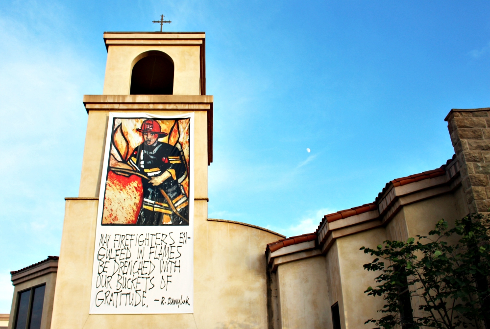 Fr. Rich Danyluk and Fr. Bill Moore work together to create artwork for Holy Name of Mary in San Dimas, California. Moore draws the pictures and Dayluk creates the captions. This banner thanks firefighters dealing with wildfires all over California.