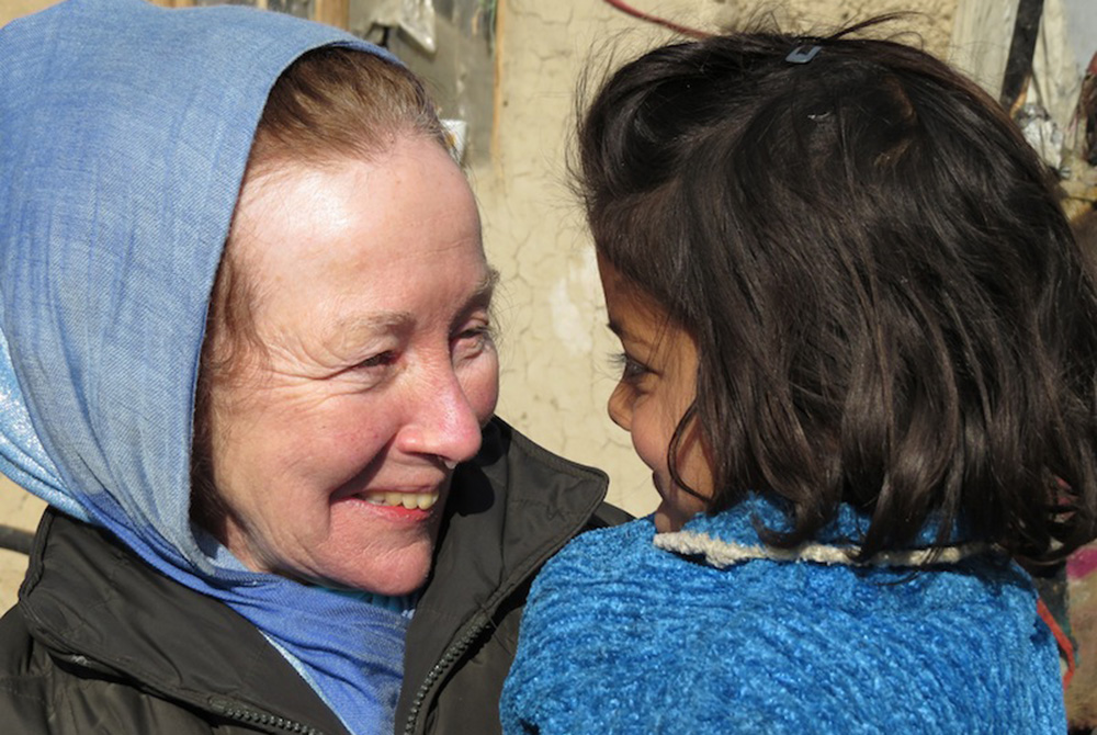 Kathy Kelly with a child at a refugee camp in Afghanistan in 2014 Kathy Kelly holds a child at the Chamin-E-Babrak refugee camp in Kabul, Afghanistan, in January 2014, a few days after the child had been saved from a burning tent, during a fire that destroyed much of the camp. (Abdulhai Darya)