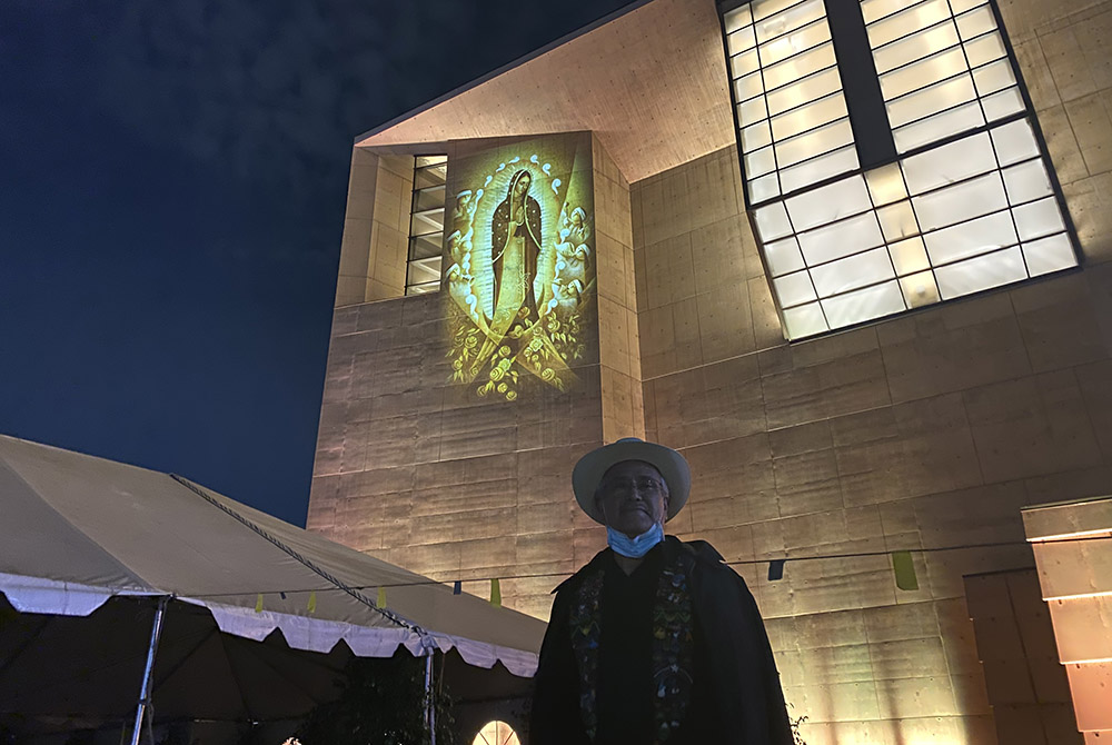 Artist Lalo Garcia stands in front of his 2013 painting of Our Lady of Guadalupe, Cihualpilli Tonantzin (“Noble Little Indian, Our Mother”), projected in light onto the outer wall of the Cathedral of Our Lady of the Angels, Dec. 9 in downtown Los Angeles.