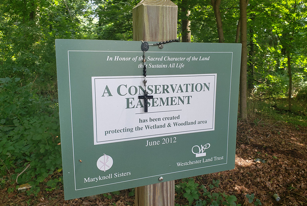 A rosary rests on a sign indicating the Maryknoll Sisters' conservation easement. (EarthBeat photo/Chris Herlinger)