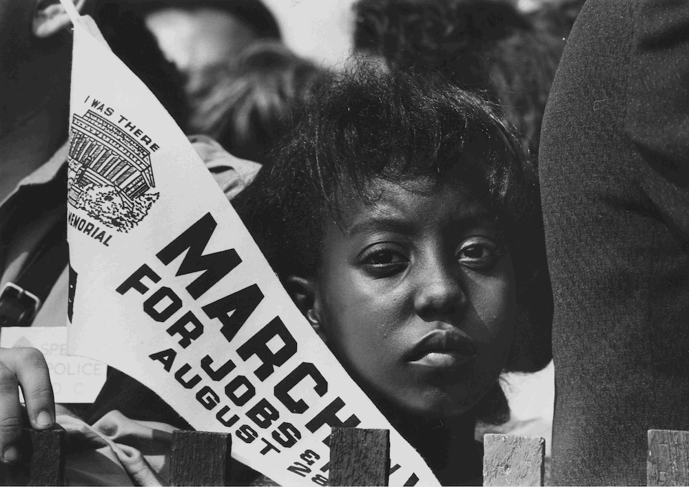 A young woman at the March on Washington for Jobs and Freedom holds a commemorative banner Aug. 28, 1963. (National Archives/U.S. Information Agency, Press and Publications Service/Rowland Scherman)