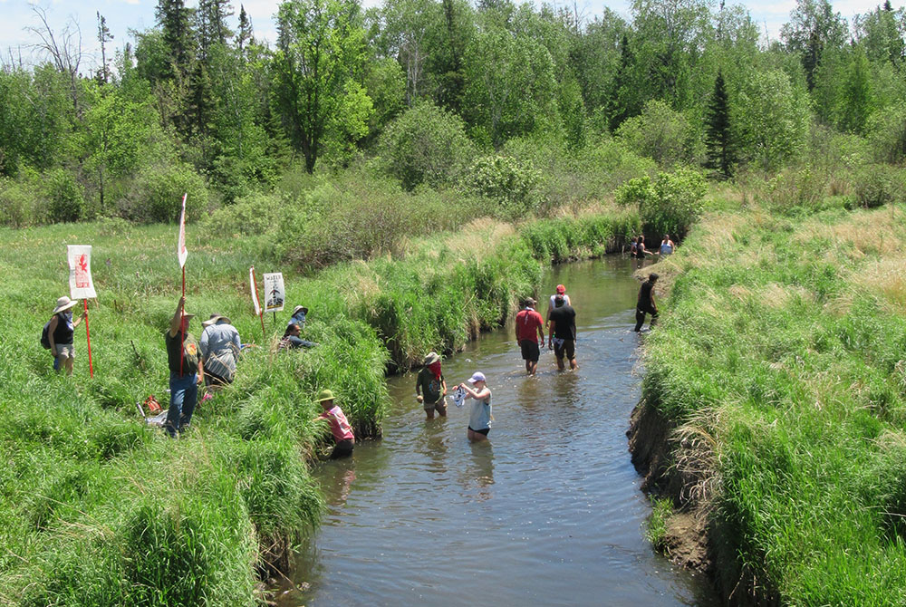 Demonstrators participating in the gathering against the Enbridge Line 3 pipeline June 7 take a break from the heat in the headwaters of the Mississippi River. (Claire Schaeffer-Duffy)