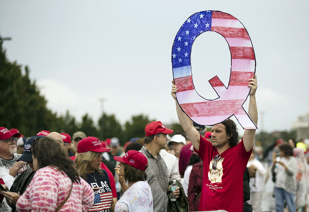In this Aug. 2, 2018, file photo, a protester holds a Q sign, referencing the fringe conspiracy theory QAnon, as he waits in line with others to enter a campaign rally with then-President Donald Trump in Wilkes-Barre, Pennsylvania. (AP/Matt Rourke, File) In this Aug. 2, 2018, file photo, a protester holds a Q sign, referencing the fringe conspiracy theory QAnon, as he waits in line with others to enter a campaign rally with then-President Donald Trump in Wilkes-Barre, Pennsylvania. (AP/Matt Rourke, File)