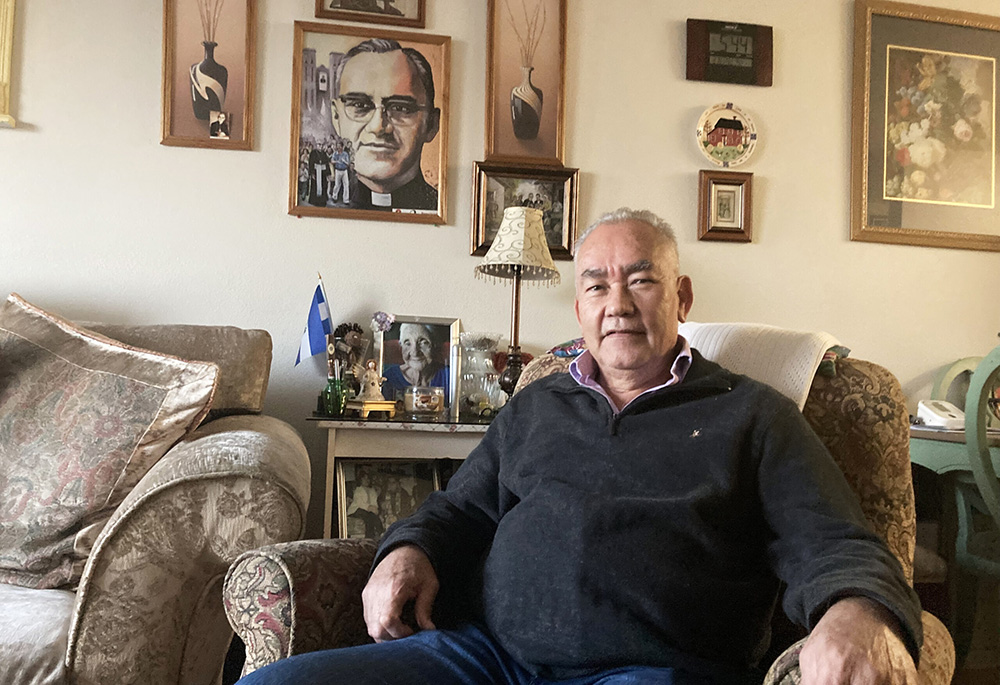 Jesús Aguilar, 65, sits for a portrait in his Los Angeles home, in front of an image of St. Oscar Romero. (RNS photo/Alejandra Molina)